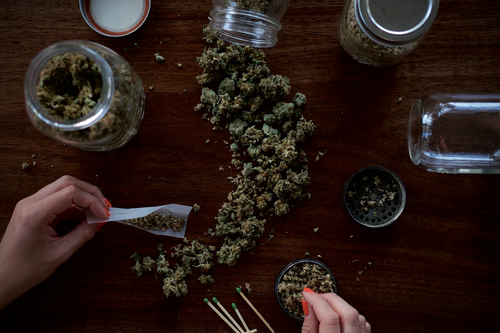 womanโs hands on a table with cannabis rolling a joint